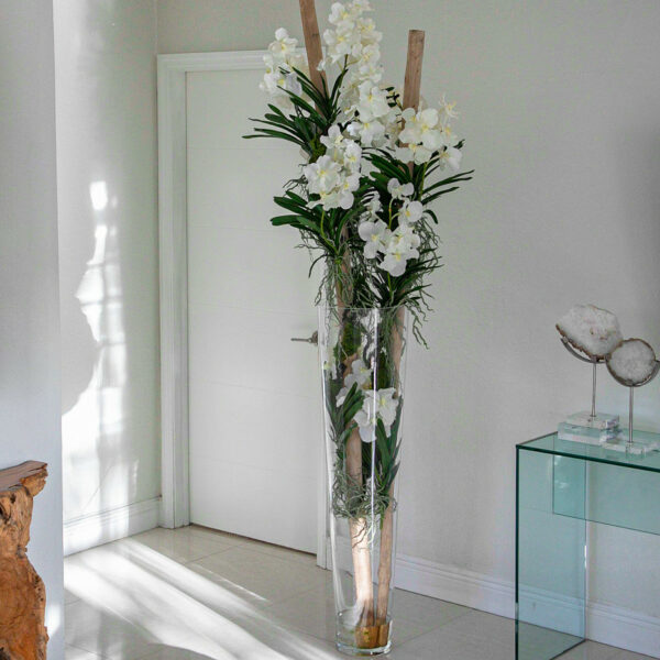 Orquídeas Vanda blancas y madera flotante dentro de un gran cilindro cónico de vidrio.